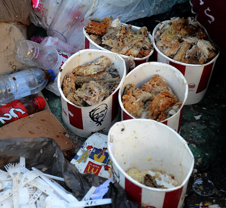 Discarded fried chicken in food containers beside discarded packaging