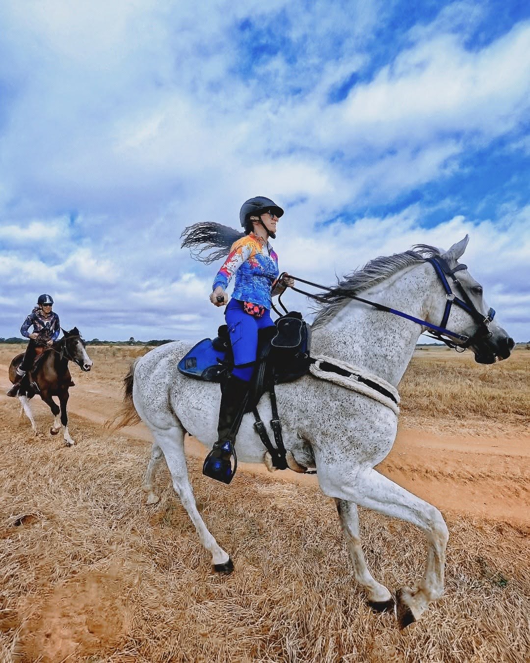 Rider wearing a colorful illustrated shirt and blue riding bottoms on a gray horse outdoors