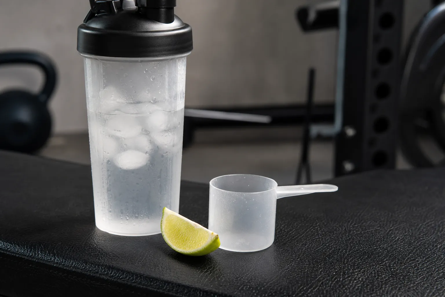 Clear shaker with ice, water and a scoop on a gym bench