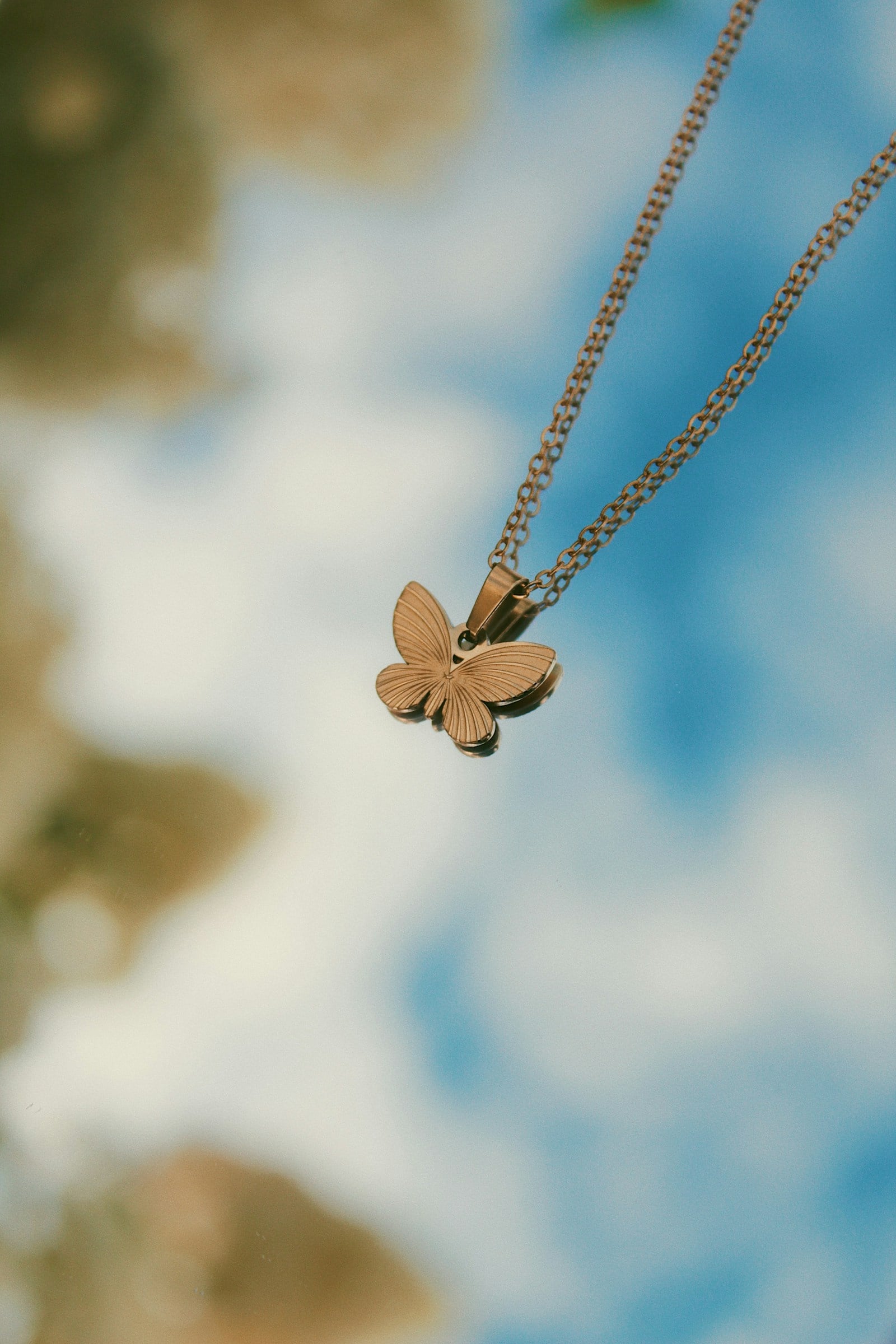 Gold butterfly pendant necklace against a soft sky