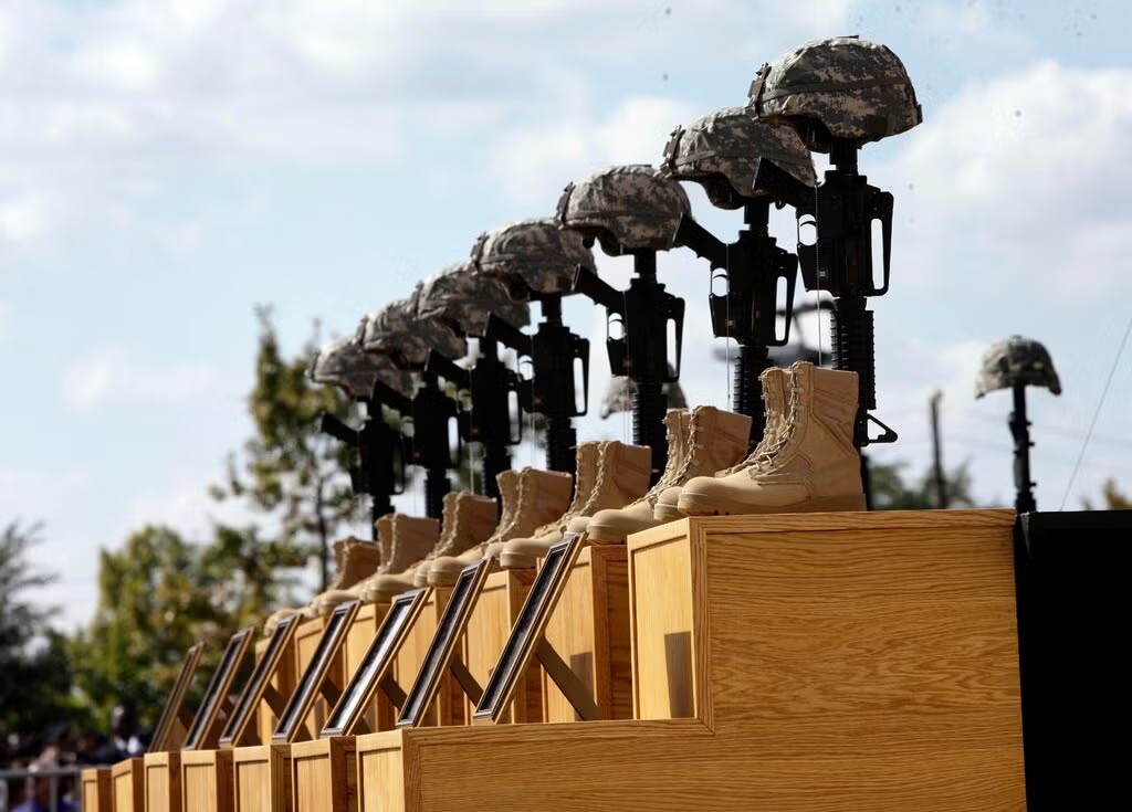 Helmets, rifles, boots, and framed photographs arranged in a military memorial