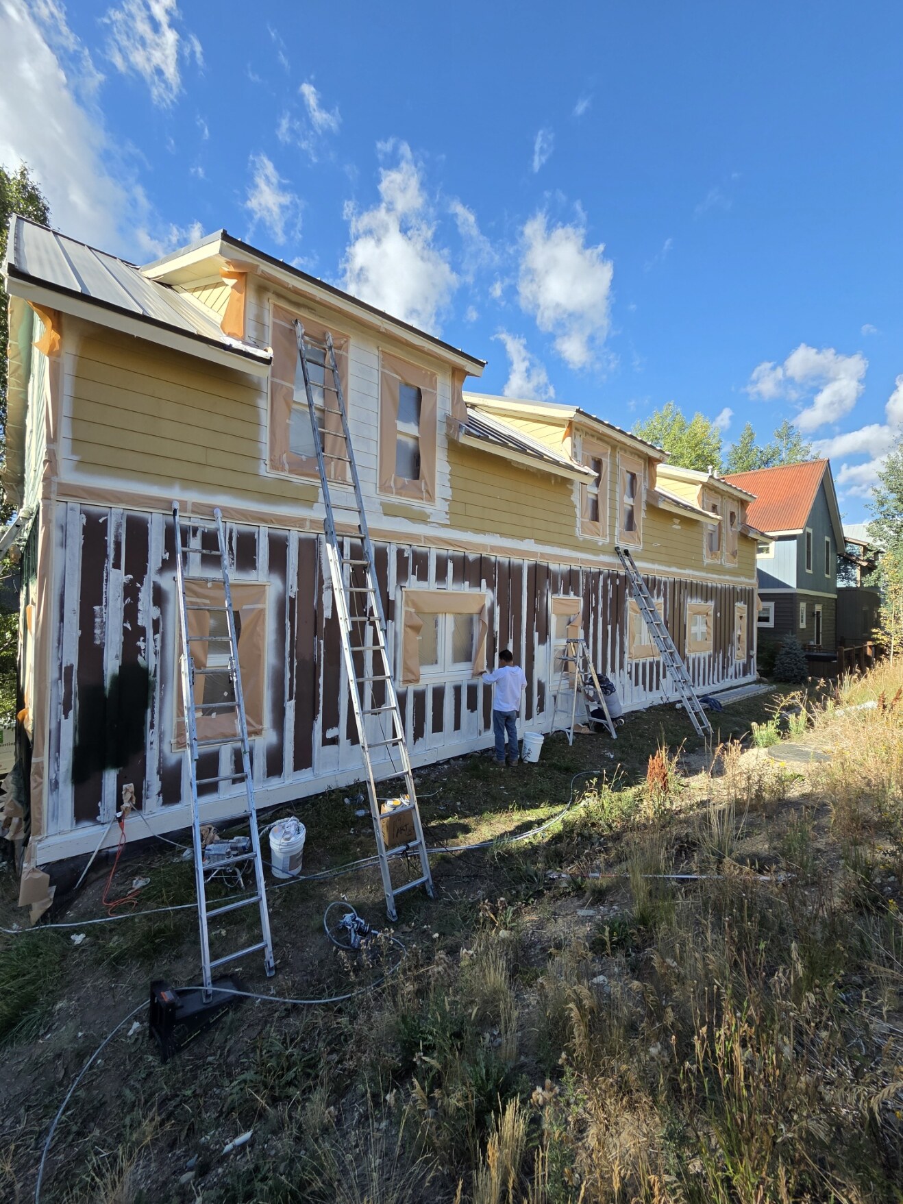 Exterior home masked and prepared for painting, with ladders in place