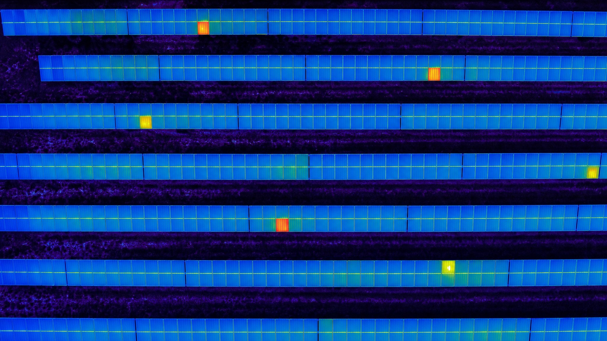 Thermal aerial view of a solar panel array with several hot modules highlighted in orange and red