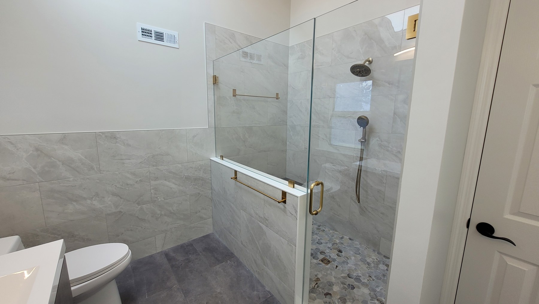 Completed Collegeville bathroom with a glass-enclosed tiled shower, recessed niche, patterned shower floor, toilet, and tile wainscoting