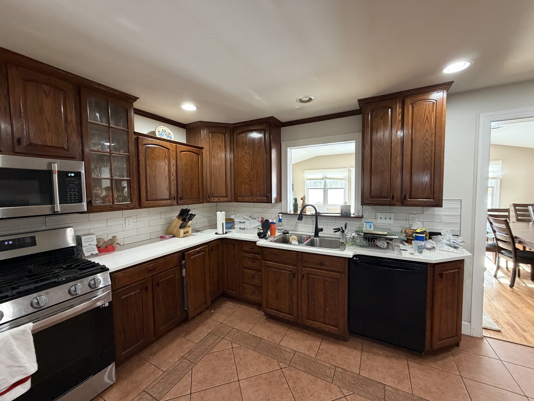 Original King of Prussia kitchen with wood-finish cabinets, light countertops, a corner sink, and brown tile flooring