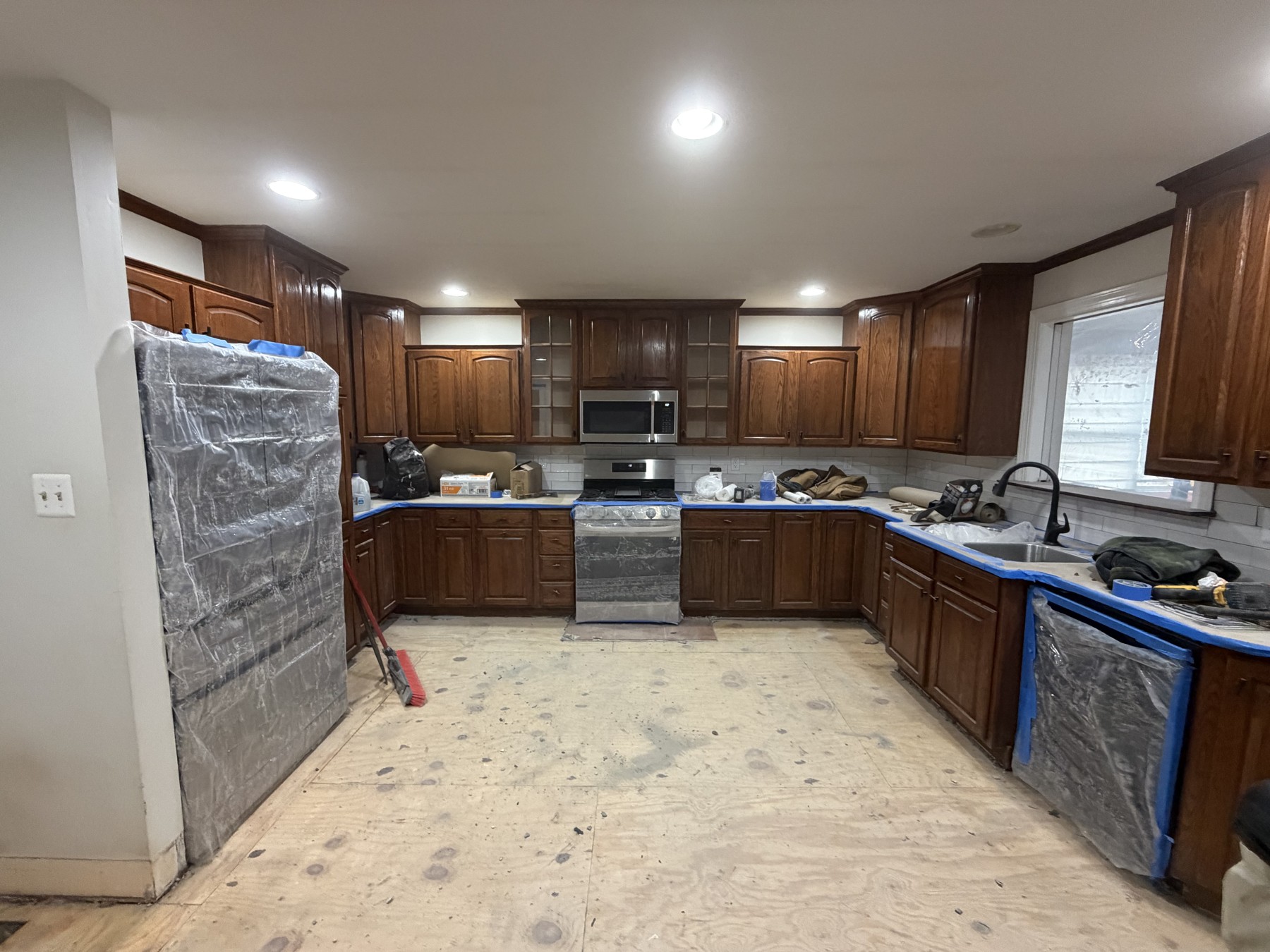 Kitchen during the refresh with exposed subfloor, original wood-finish cabinets, and protected appliances and countertops