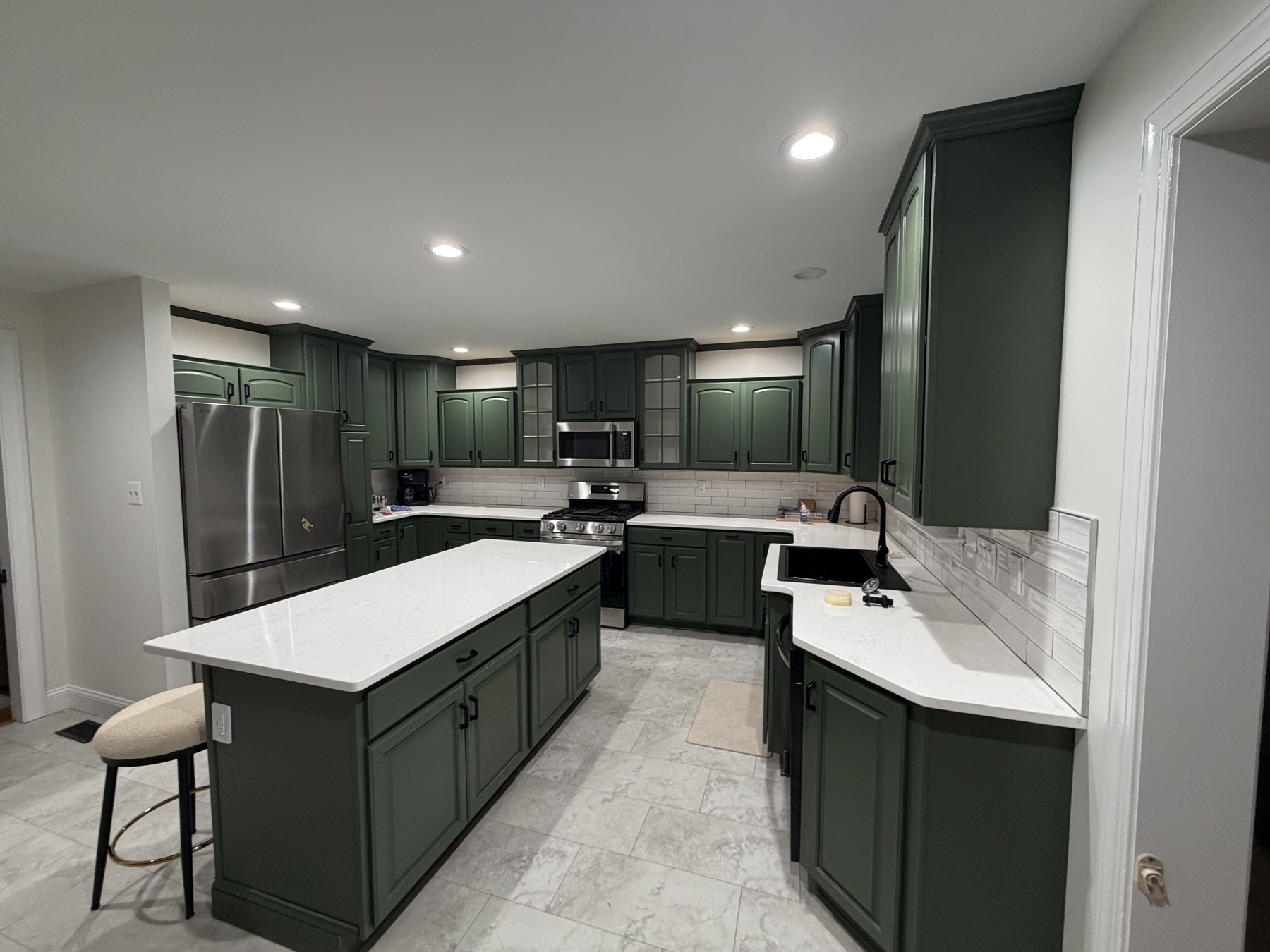 Green repainted existing kitchen cabinets with black hardware, a central island, light countertops, and new flooring