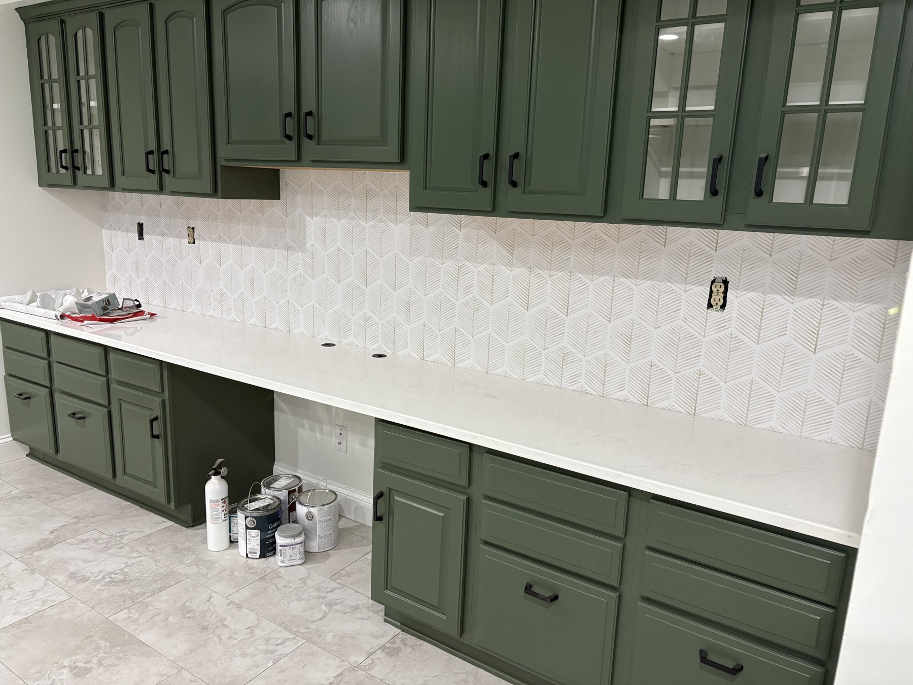 Repainted green upper and lower cabinets with black handles, a light countertop, and paint cans on the floor