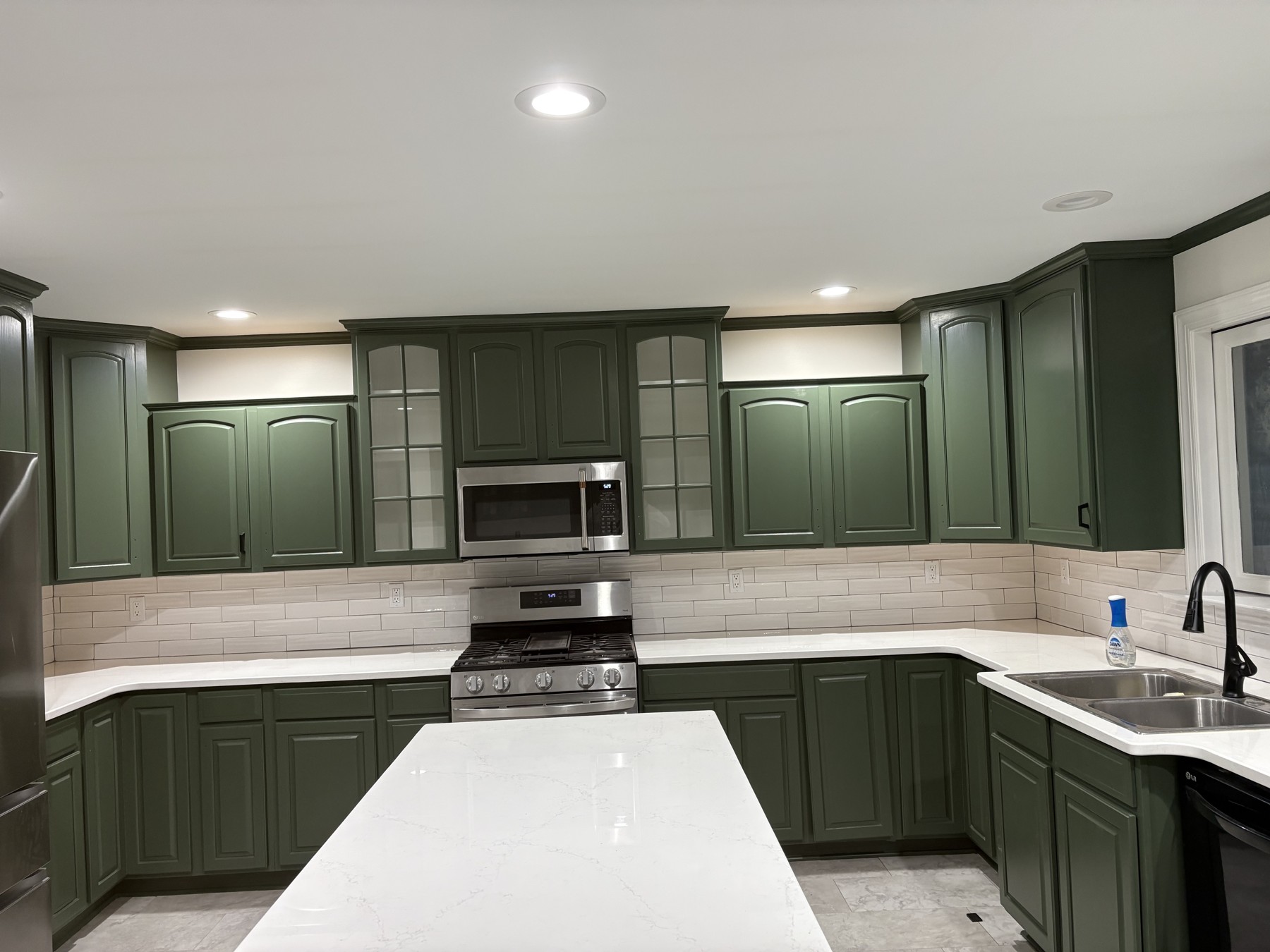 Green repainted kitchen cabinets around a range and sink, with the island countertop in the foreground