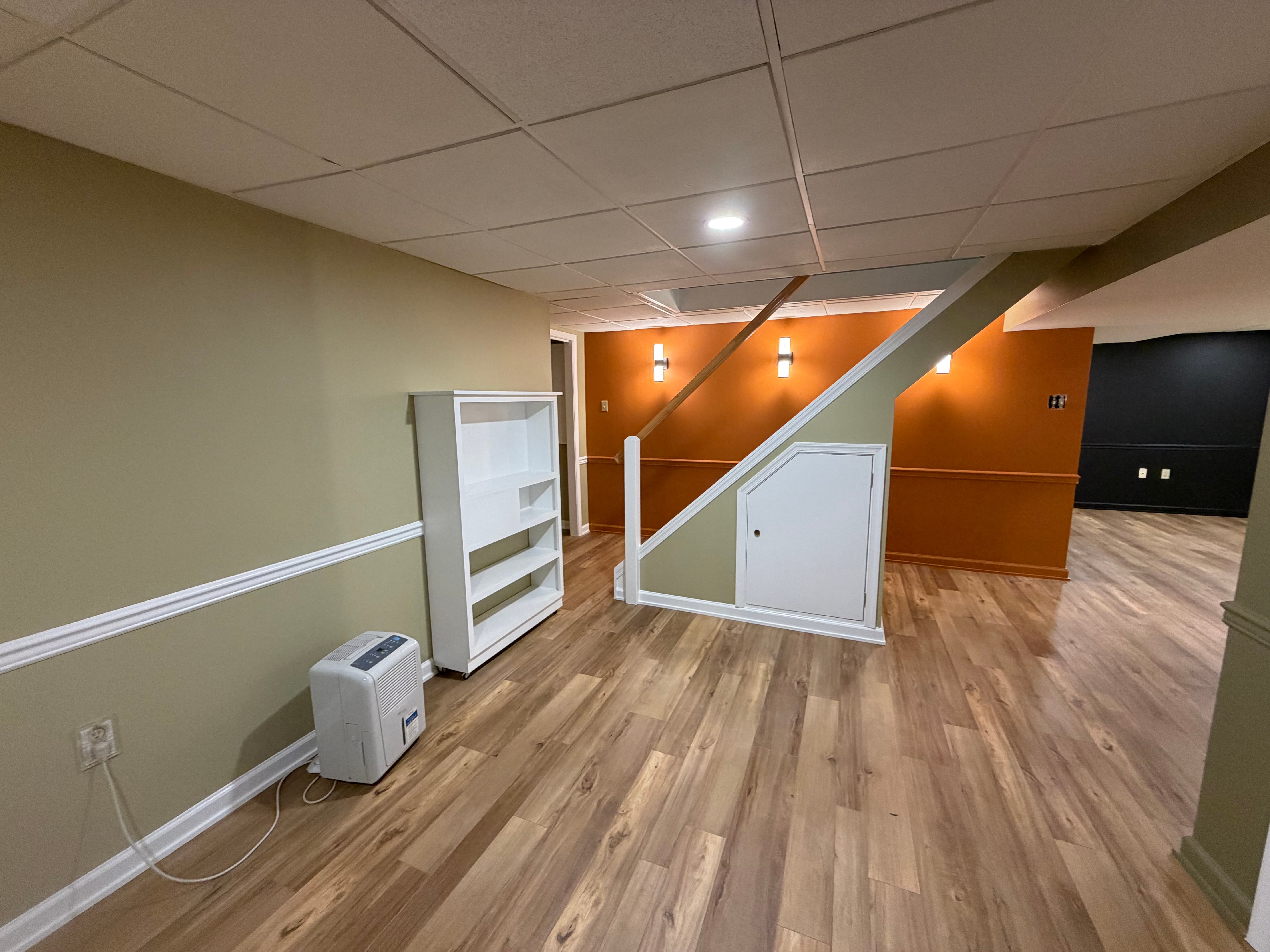 Finished Pottstown basement with white bookshelf, staircase, orange accent wall, and LVP flooring