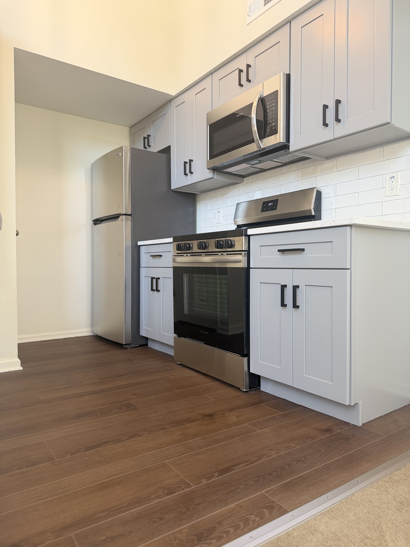Gray kitchen cabinets with black handles, stainless steel refrigerator, range, microwave, and new flooring in Royersford