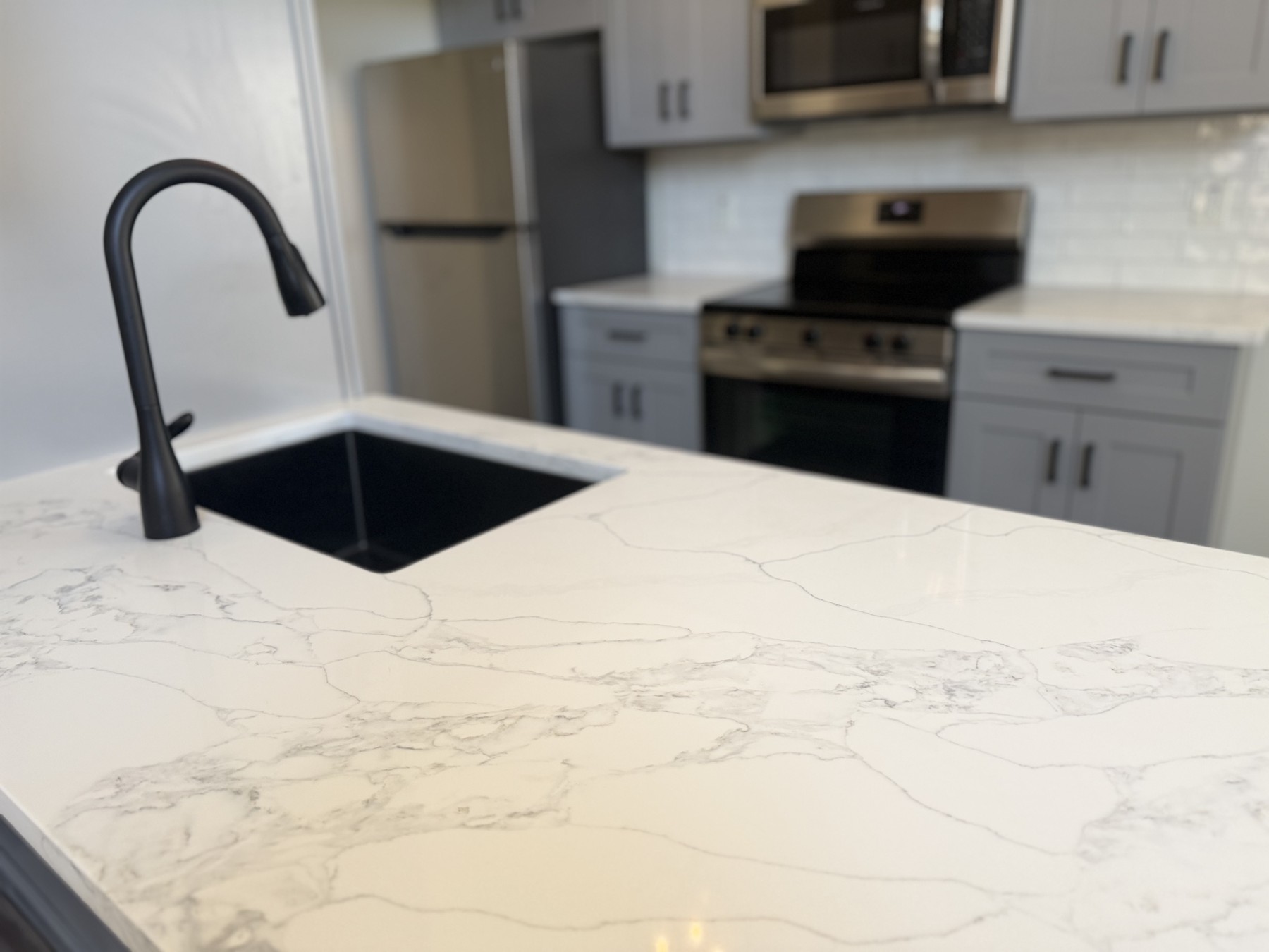 Veined quartz countertop surrounding a black sink and faucet, with gray cabinets and appliances in the background