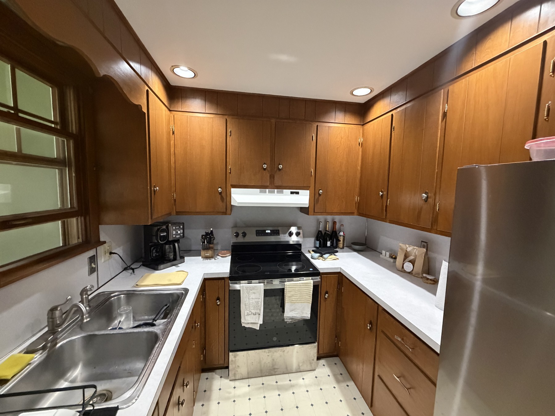 Original kitchen sink and range area with wood-finish cabinets and older countertops