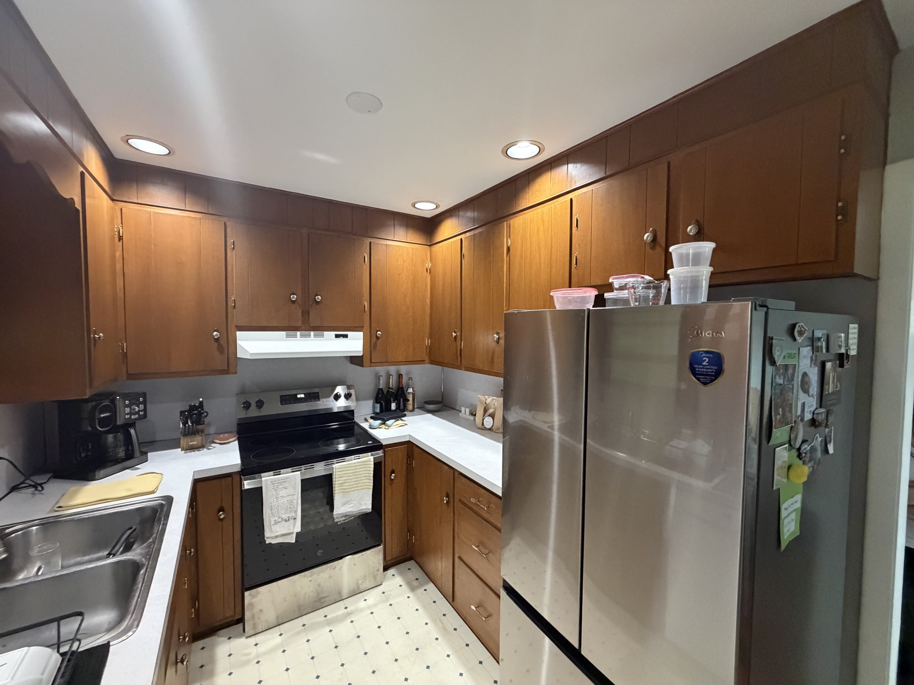 Wood-finish kitchen cabinets surrounding a stainless steel refrigerator and range before the refresh
