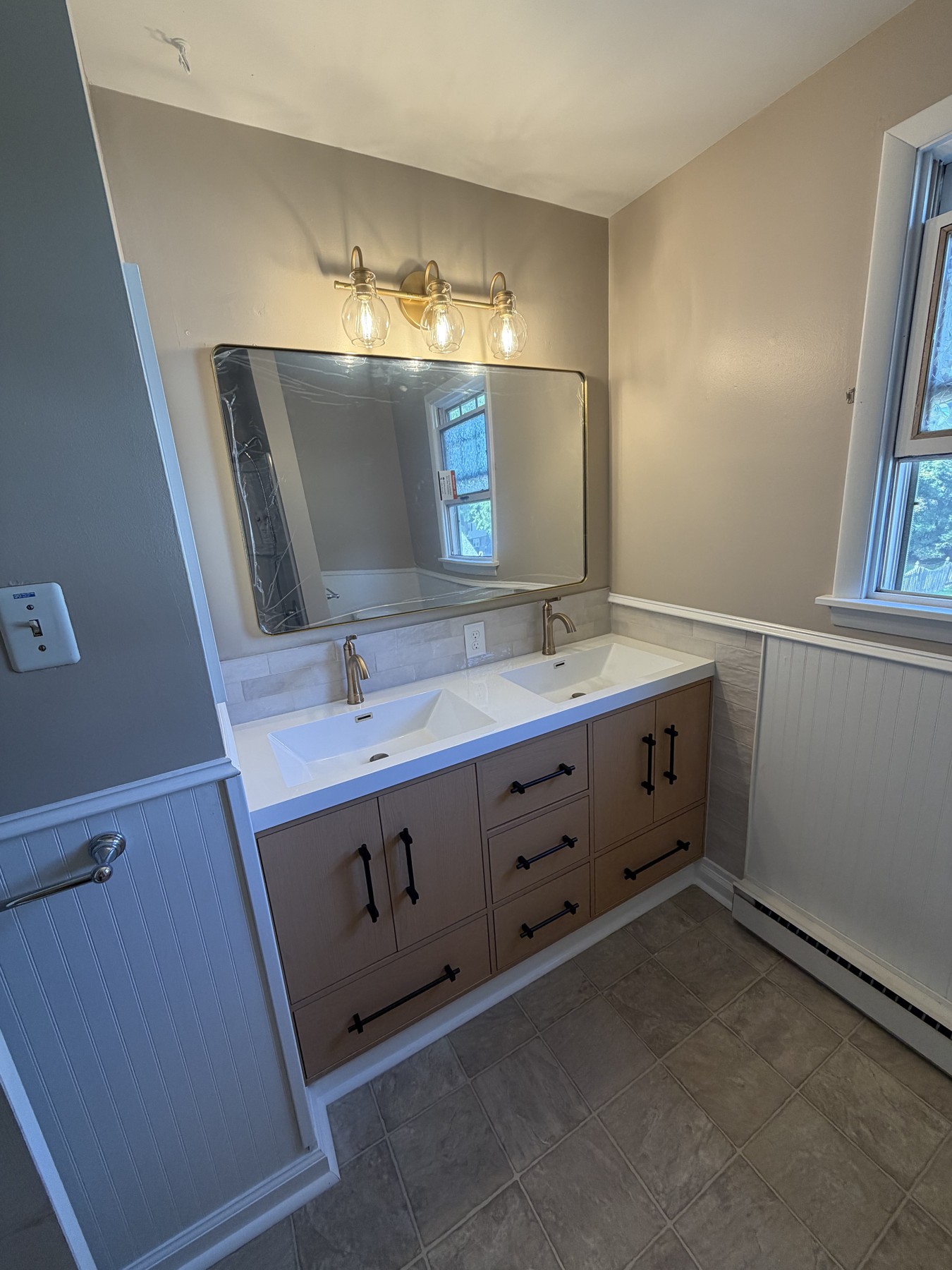 Double vanity with black pulls, light countertop, brass-toned fixtures, and tile backsplash in the main bathroom