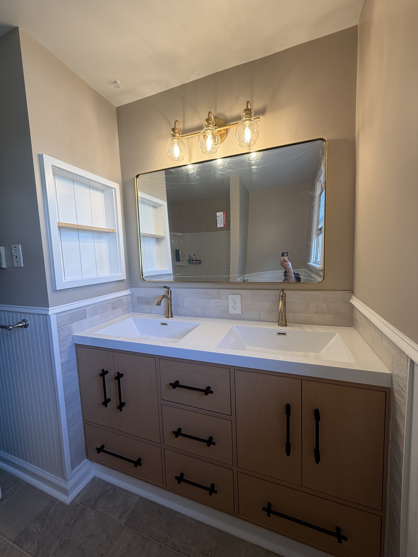 Main bathroom with a light wood double vanity, two sinks, brass-toned faucets, a large mirror, and tile backsplash