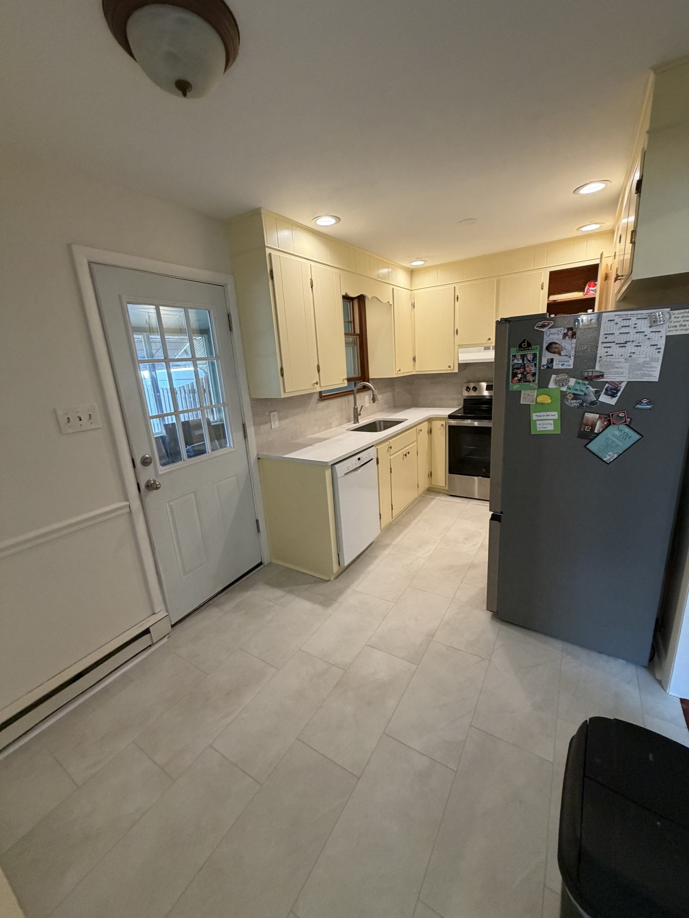 Refreshed kitchen with pale yellow cabinets, light flooring, tile backsplash, and a stainless steel refrigerator