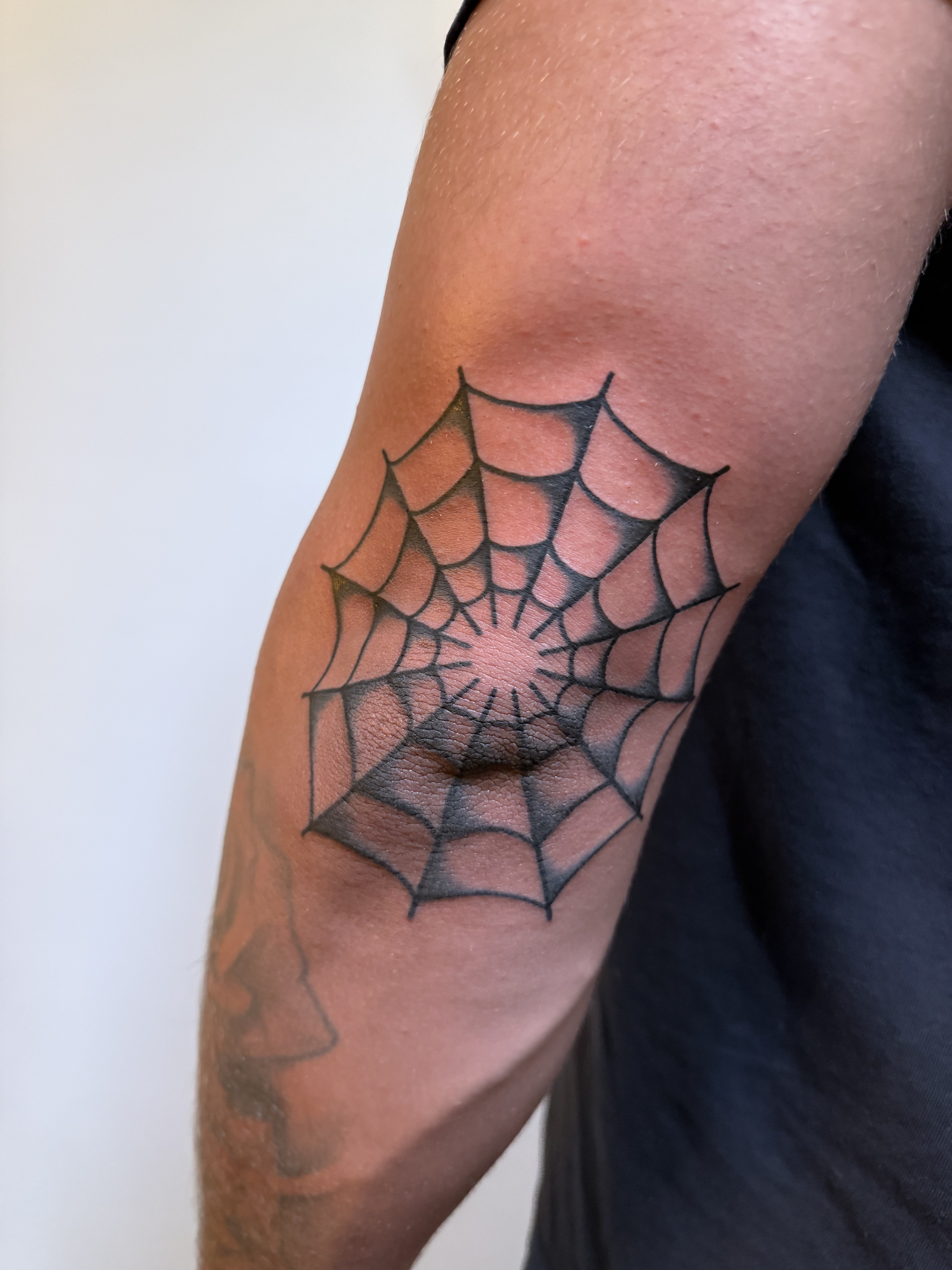 Black and gray spiderweb tattoo placed on an elbow