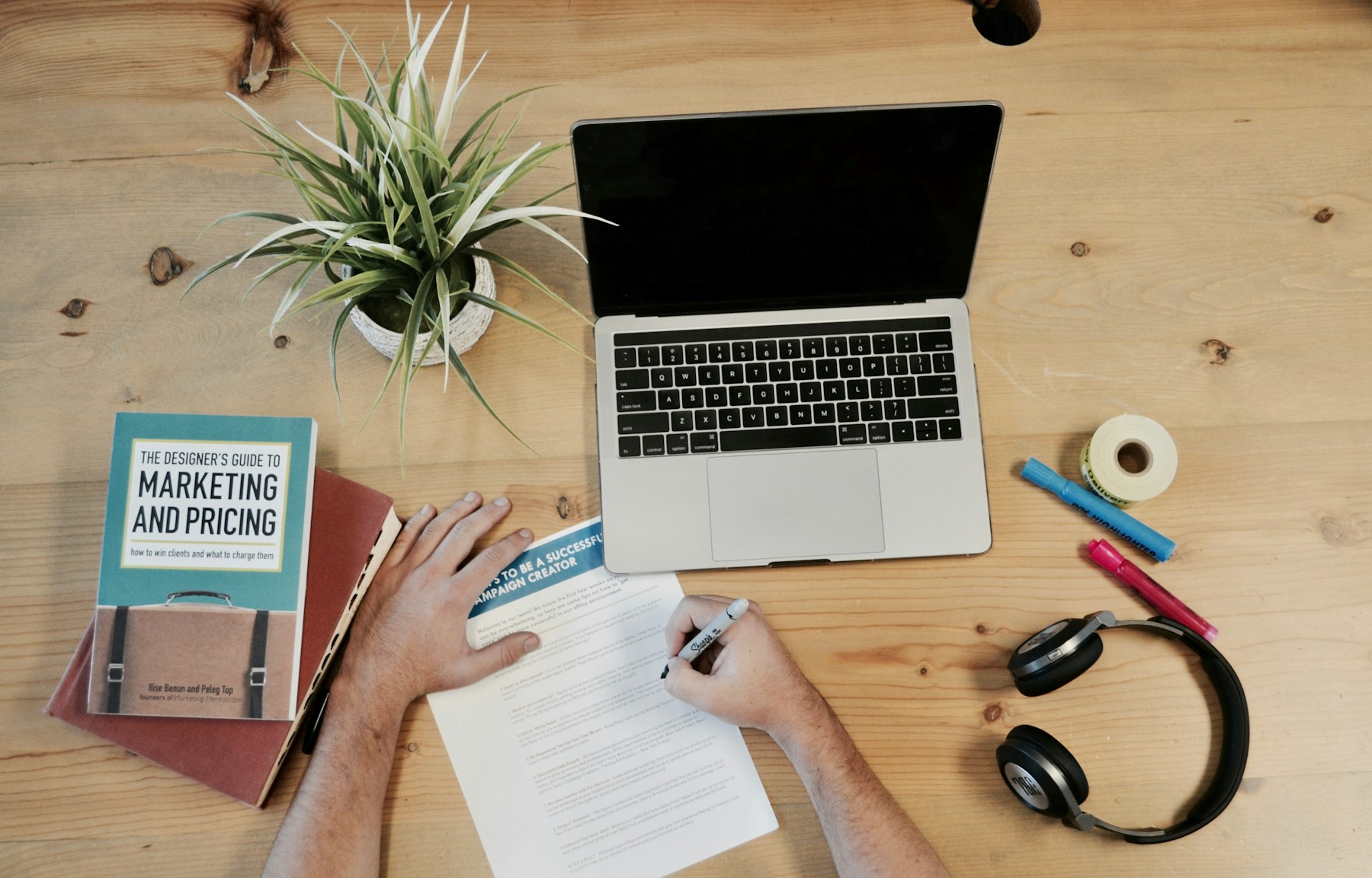 Small-business marketing desk with laptop, notebook, headphones, and planning materials