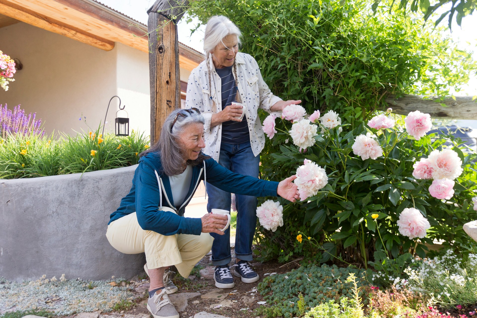 Two older women enjoying pink flowers and cups of tea in a sunny garden