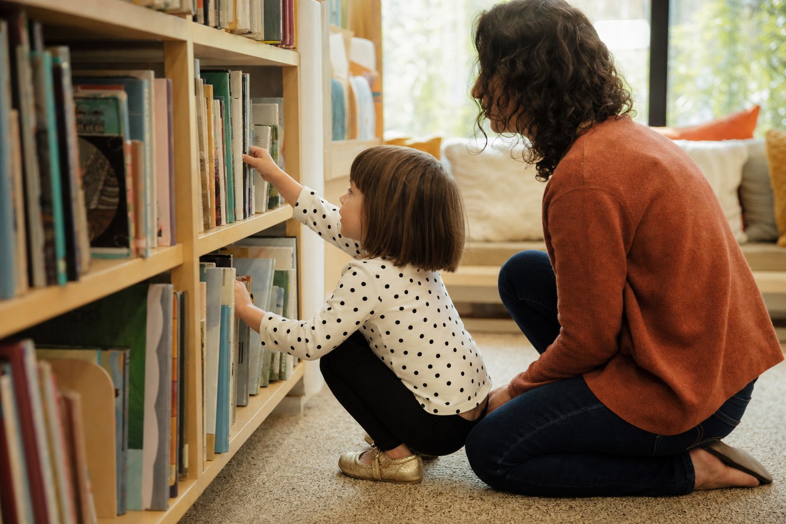 A child choosing a picture book beside an adult at a library shelf