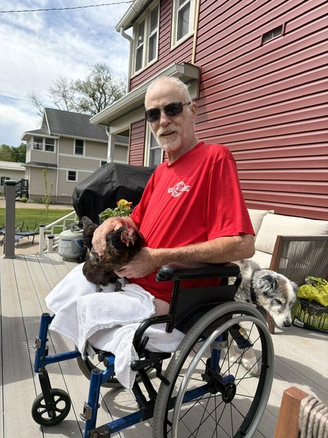 Person in a wheelchair with a cat on their lap and a dog beside them on a home deck