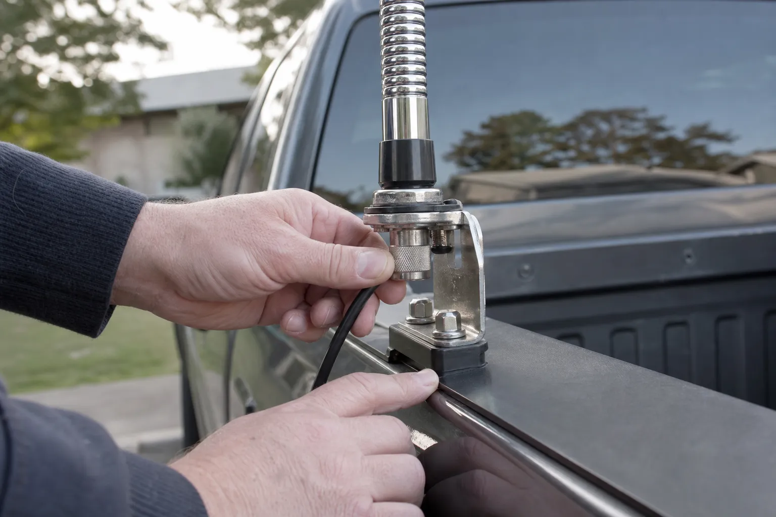 Hands checking a CB antenna mount and coax connector on a pickup truck bed rail