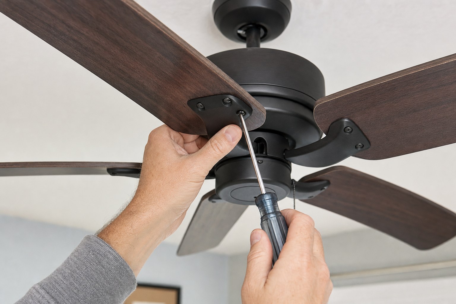 Hands checking an accessible ceiling fan blade screw with the fan switched off