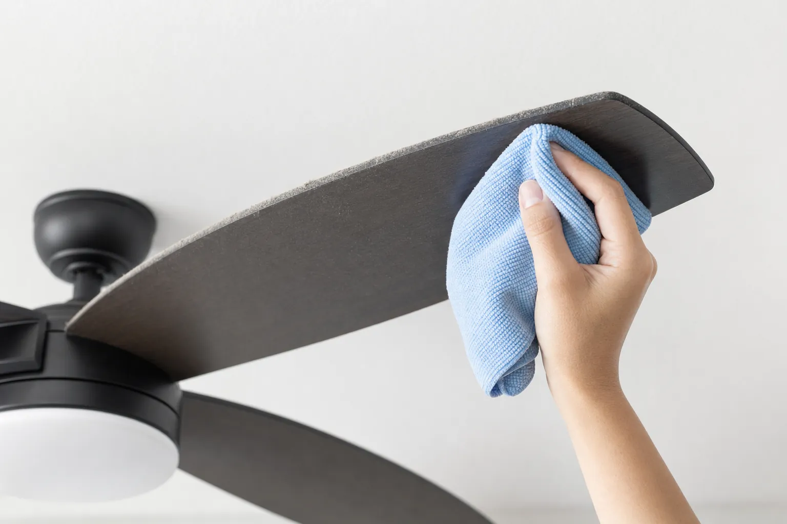 A ceiling fan blade being cleaned with a microfiber cloth