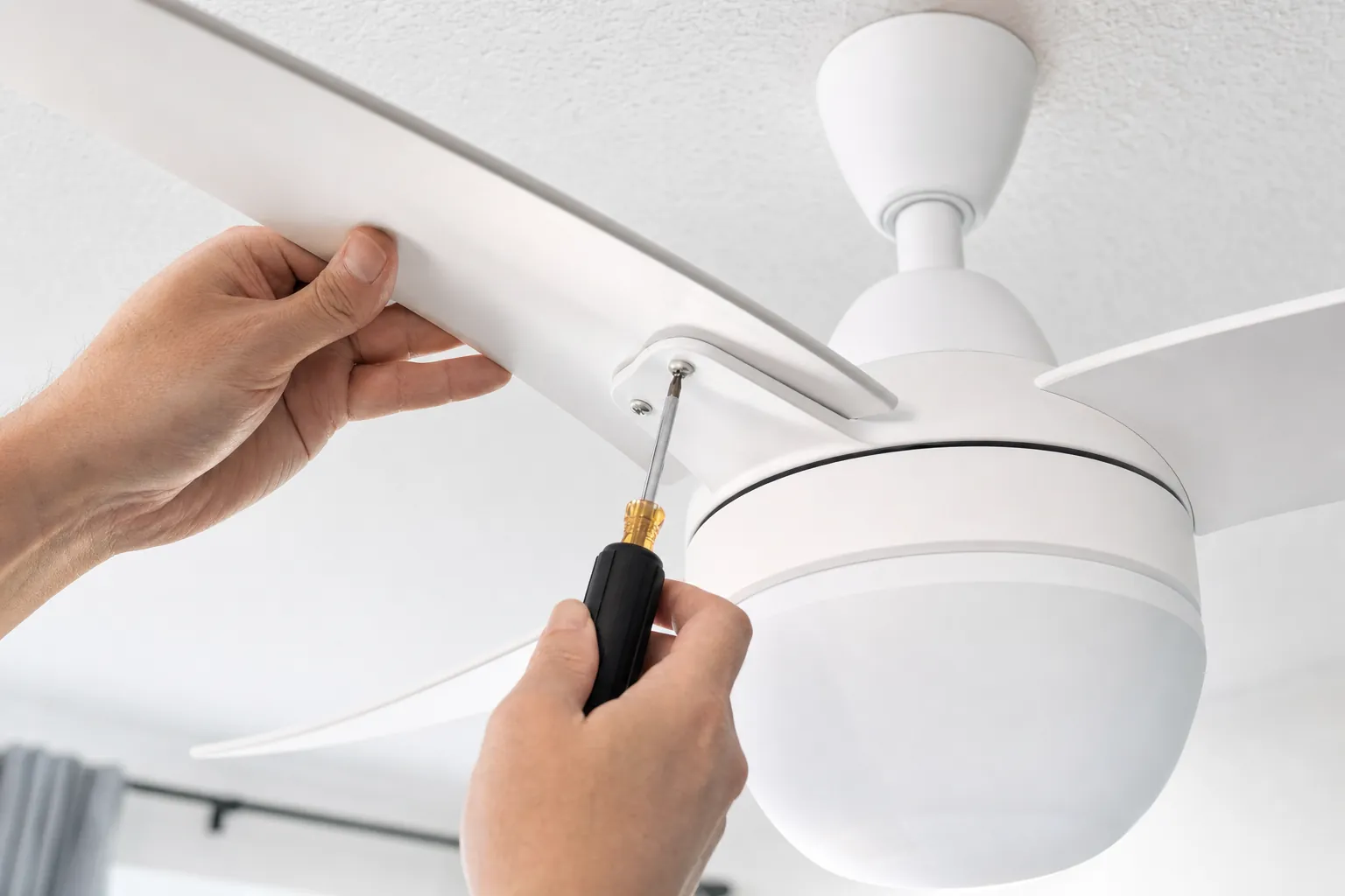 Hands carefully tightening an accessible ceiling fan blade screw