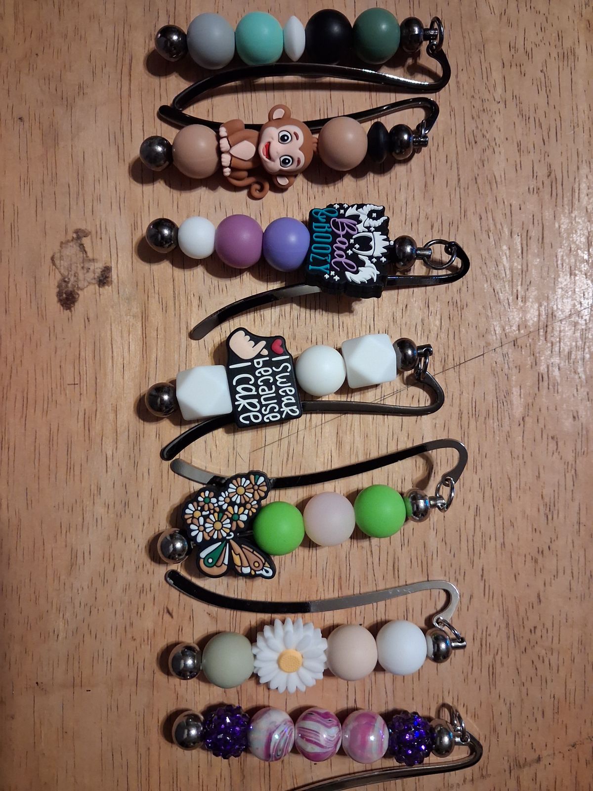 Curved metal bookmarks with colorful beaded charms including a monkey, butterfly, daisy, and purple patterned beads