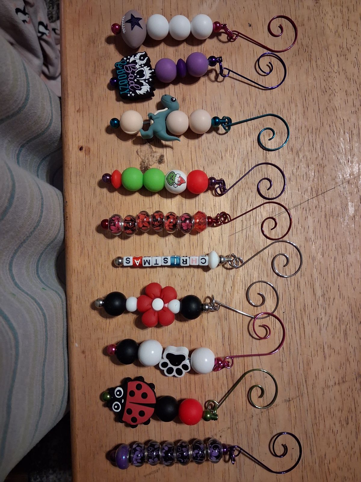 Beaded Christmas ornaments with curled metal hanging hooks, colorful beads, a flower, a paw print, and a ladybug charm on a wooden table