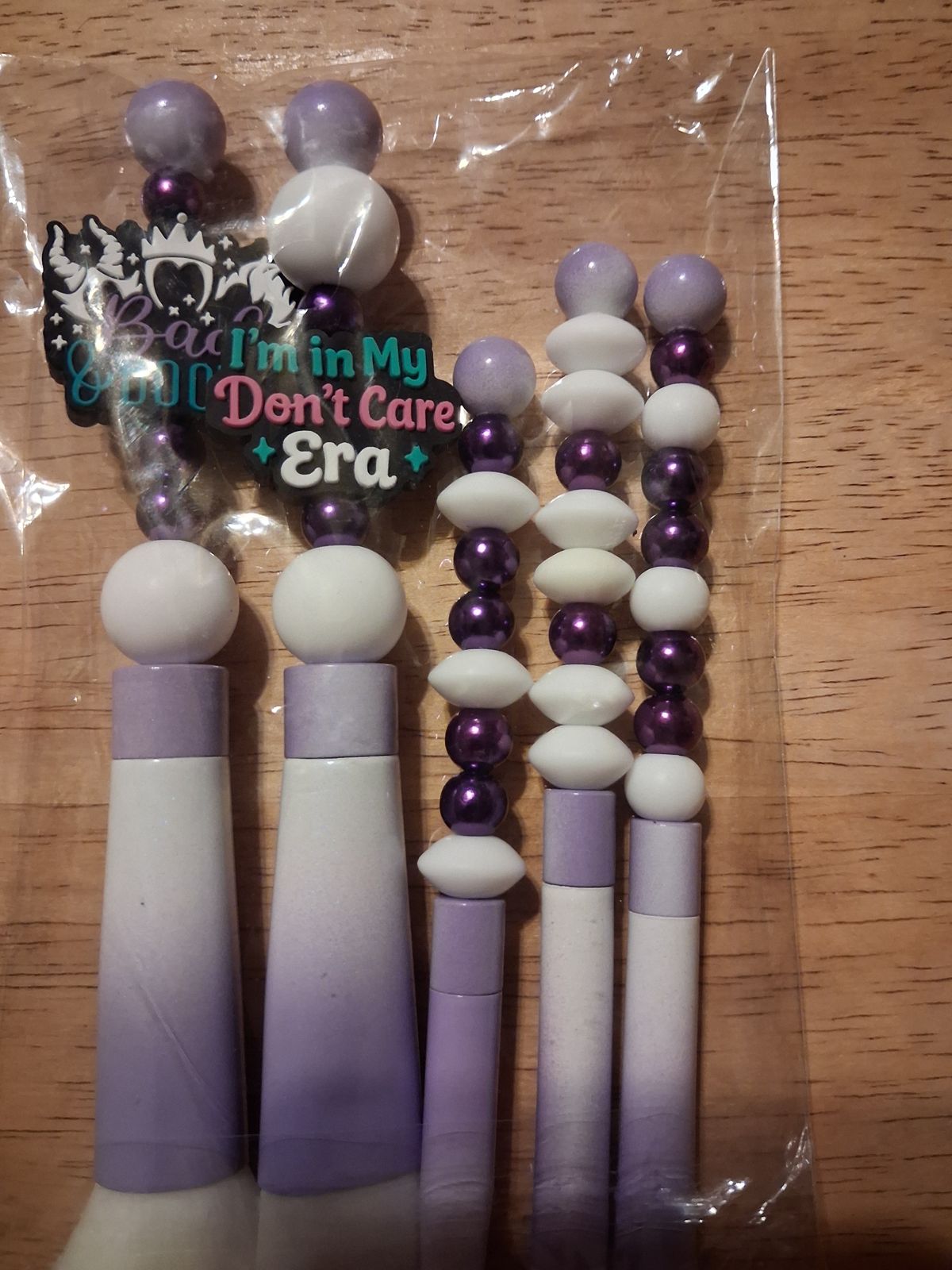 Makeup brushes with purple and white beaded handles and decorative word charms