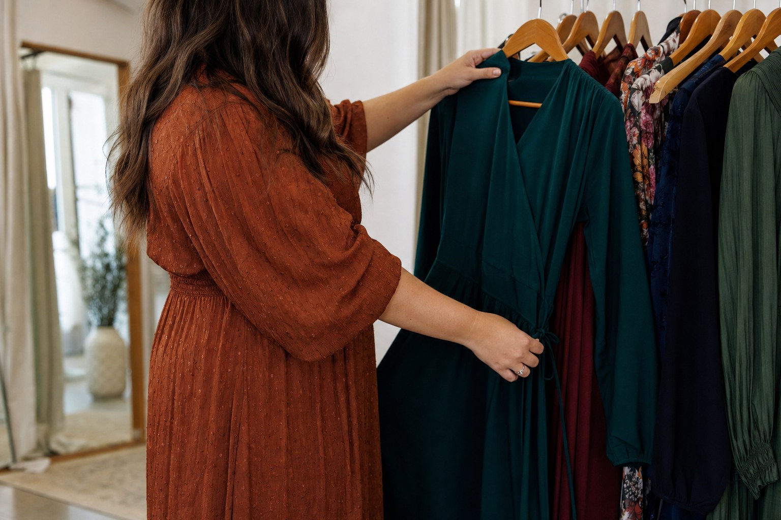 Woman choosing a deep green wrap dress from a boutique rack