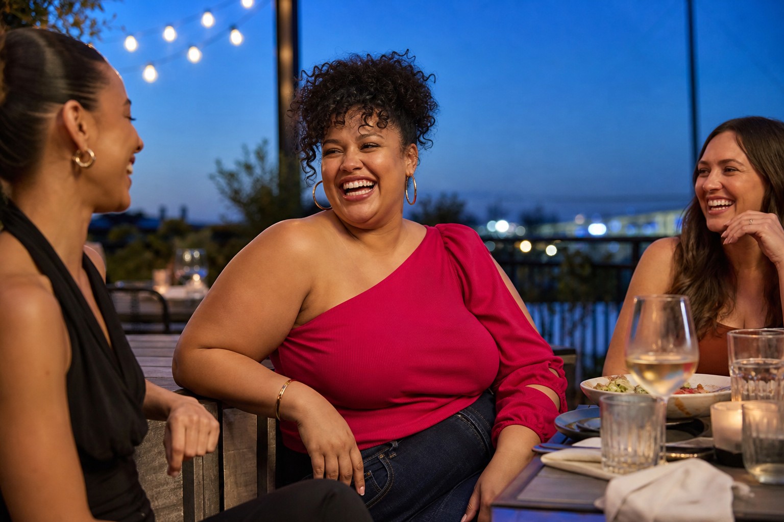 Woman in a one-shoulder top laughing with friends on a restaurant patio