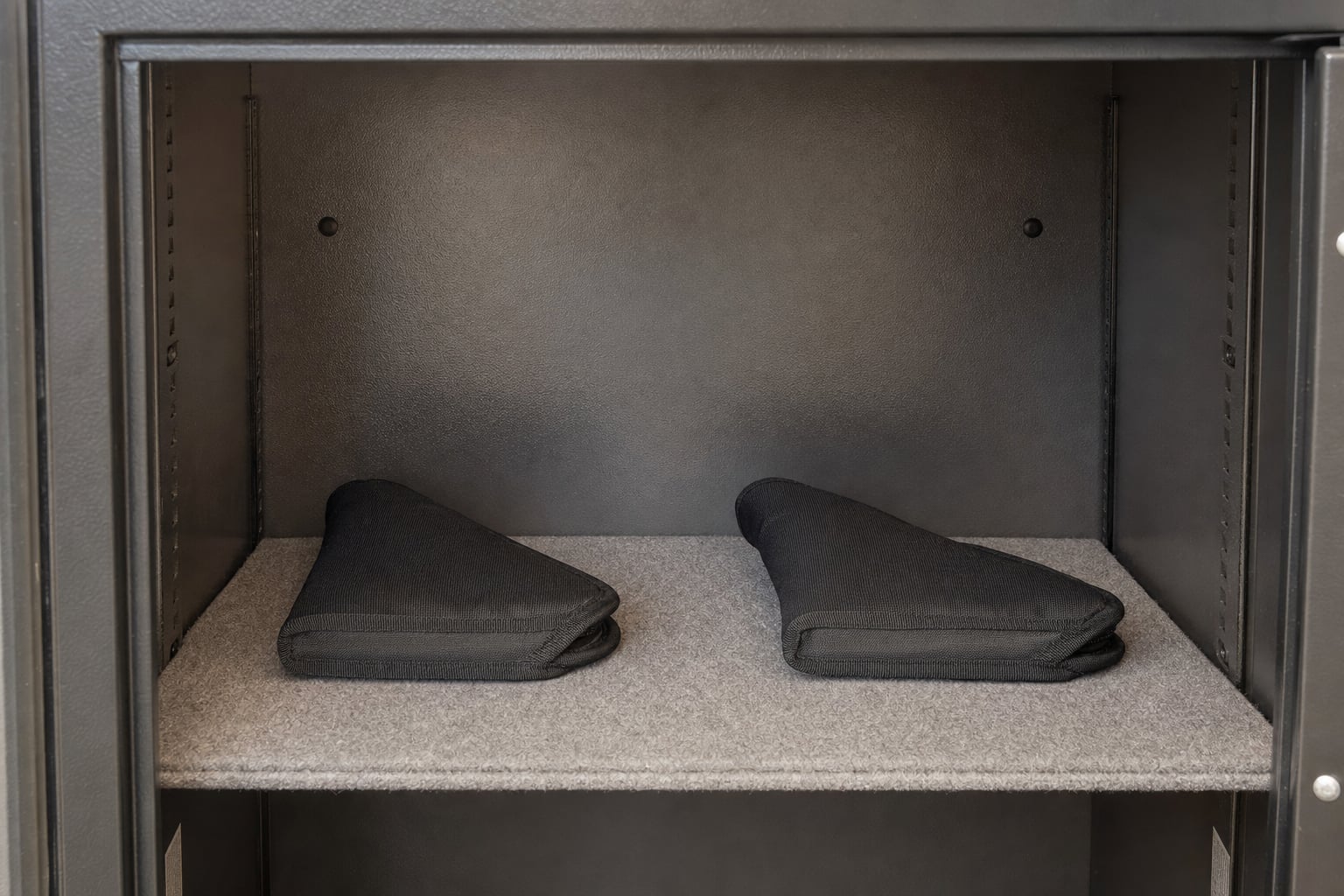 Two handguns in separate protective sleeves with clear space between them on a safe shelf