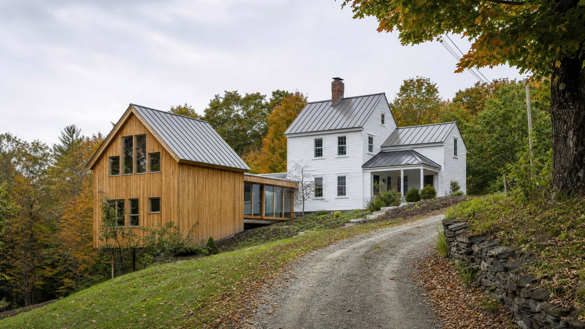 Older Vermont farmhouse connected to a contemporary timber addition on a sloped site
