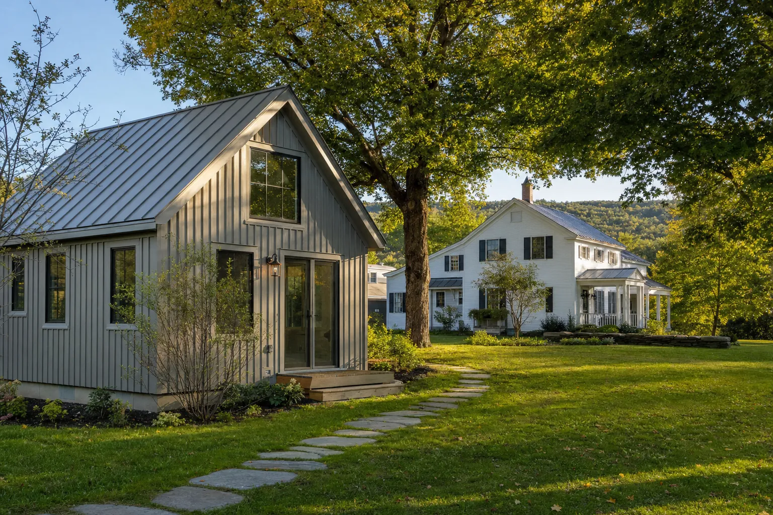 A detached backyard cottage beside a Vermont farmhouse under mature maple trees
