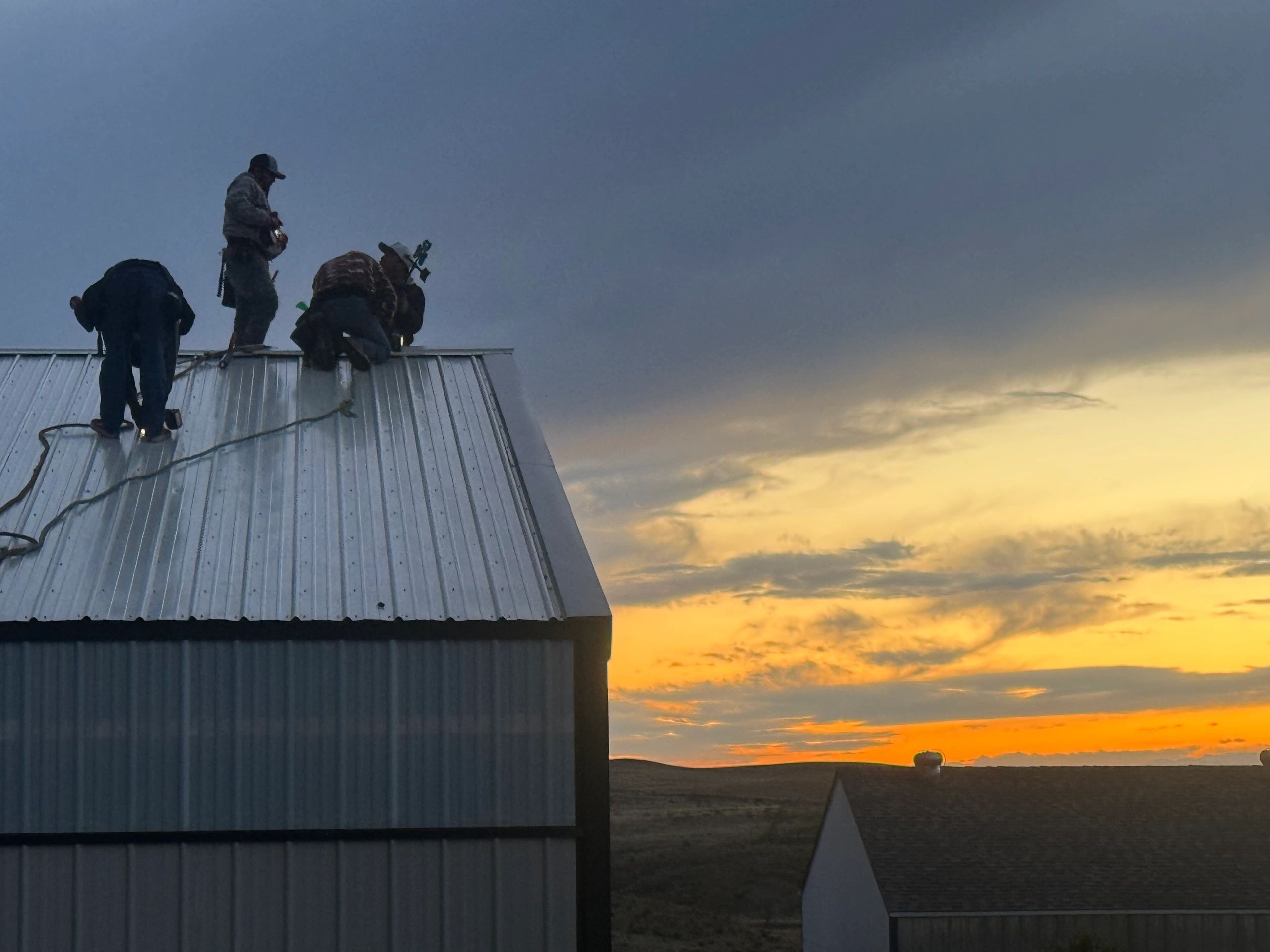 ROOF911 crew working on a metal roof at sunset