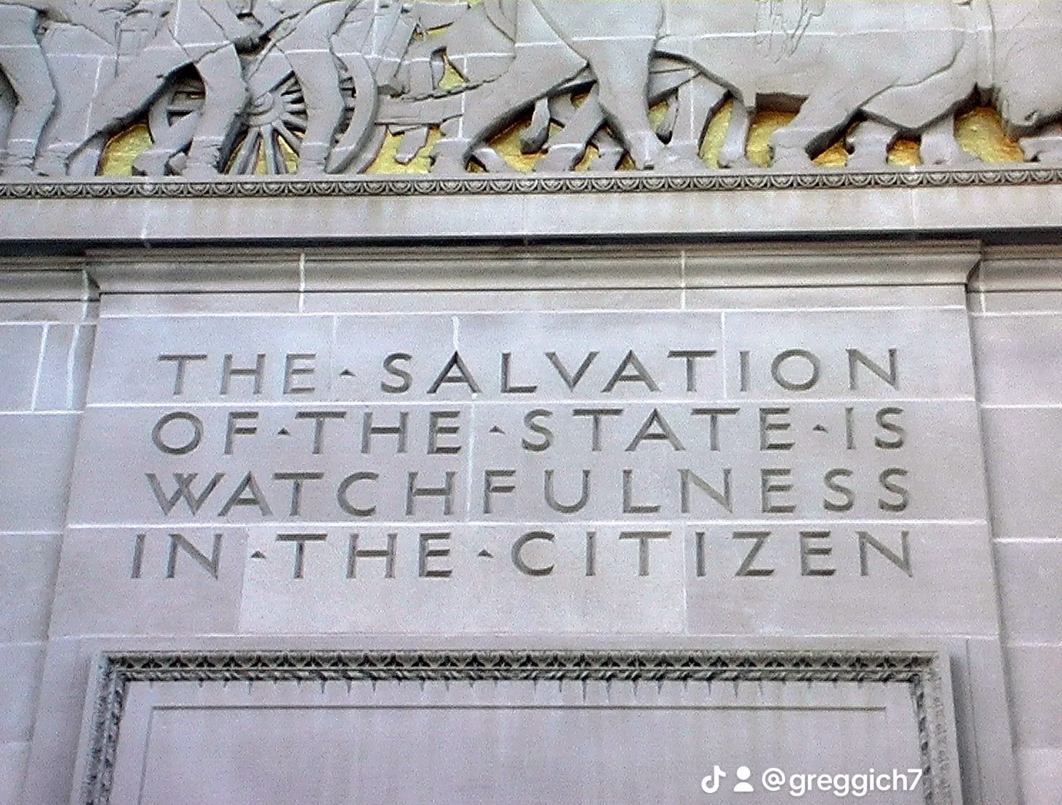Stone inscription above a Capitol doorway reading “The Salvation of the State is Watchfulness in the Citizen,” below a carved pioneer relief.