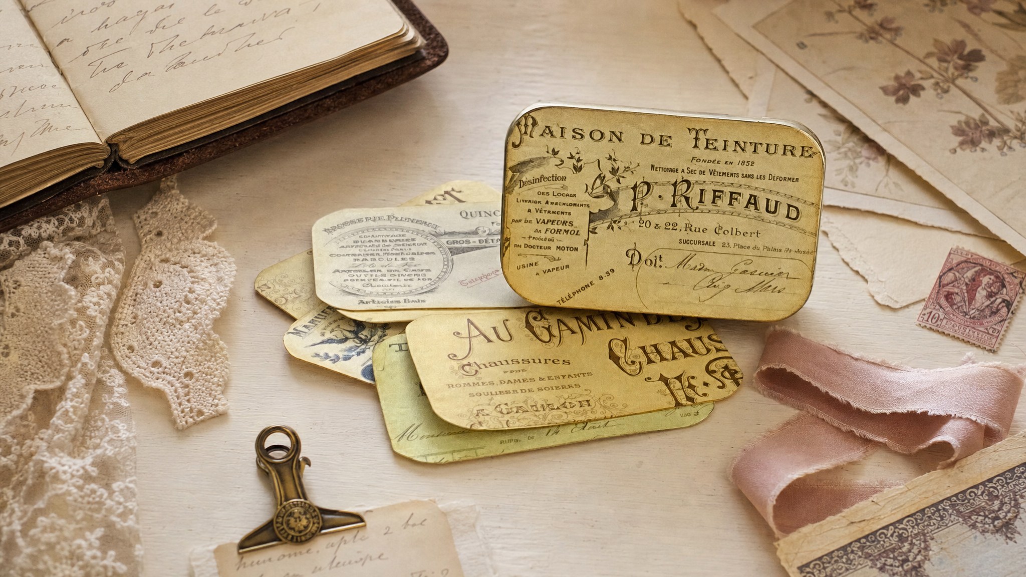 French invoice tin labels arranged with lace, vintage paper, and a handwritten notebook