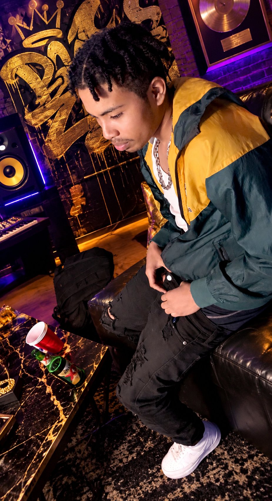 Lul Drako seated in a music studio wearing a green and yellow jacket