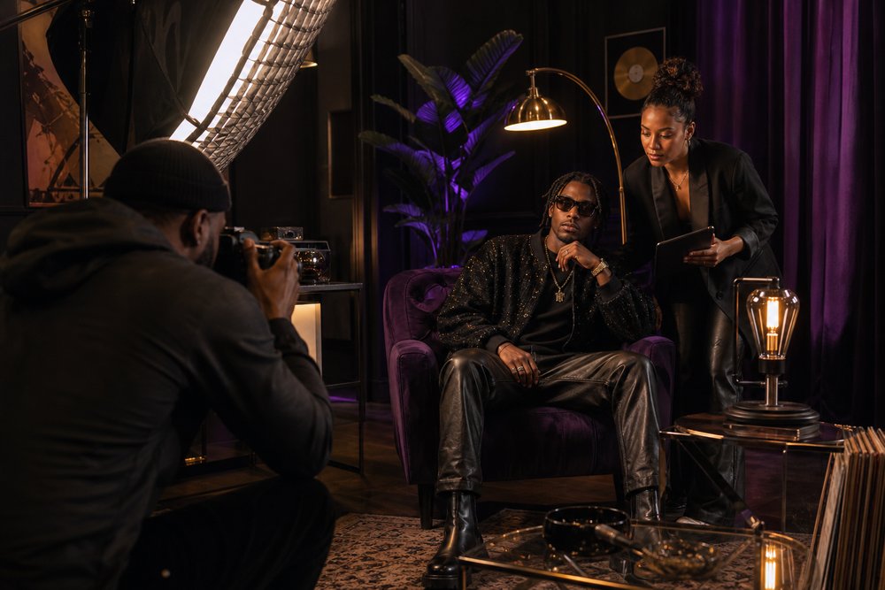 A recording artist posing for a press photographer beside a publicist on an intimate media set