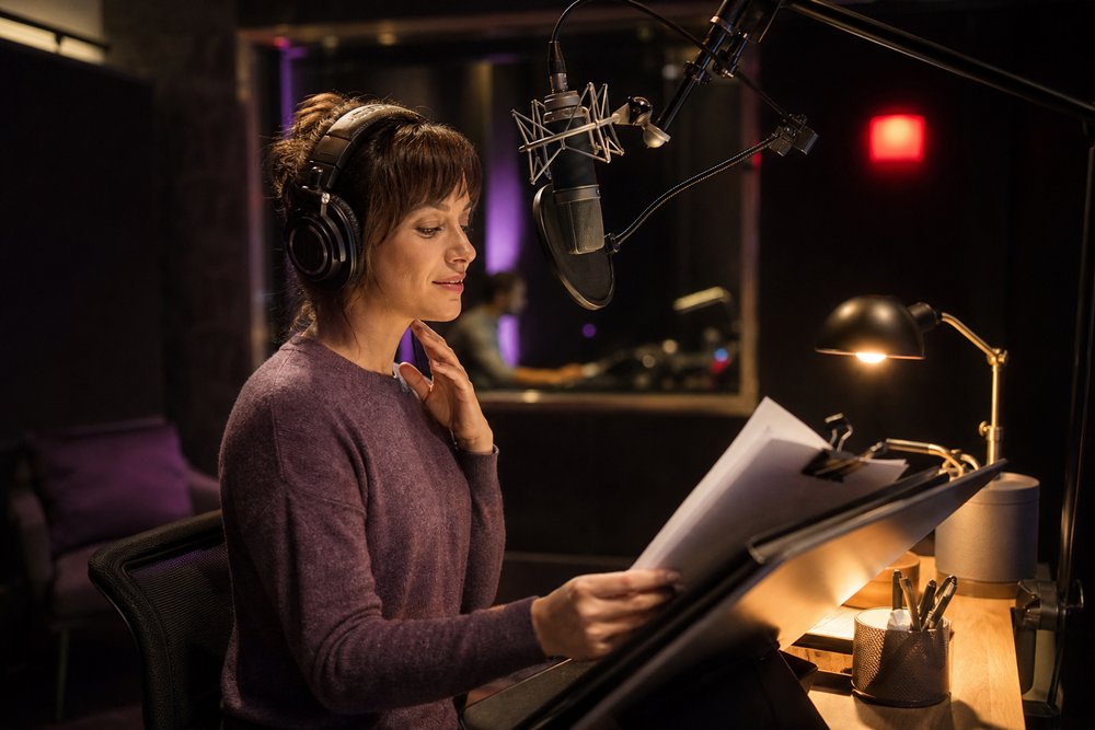 A voiceover microphone and printed advertising script in a radio recording booth with a glowing recording indicator