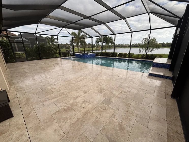 Cleaned and sealed travertine pool deck beside a pool inside a screened enclosure in Estero, FL