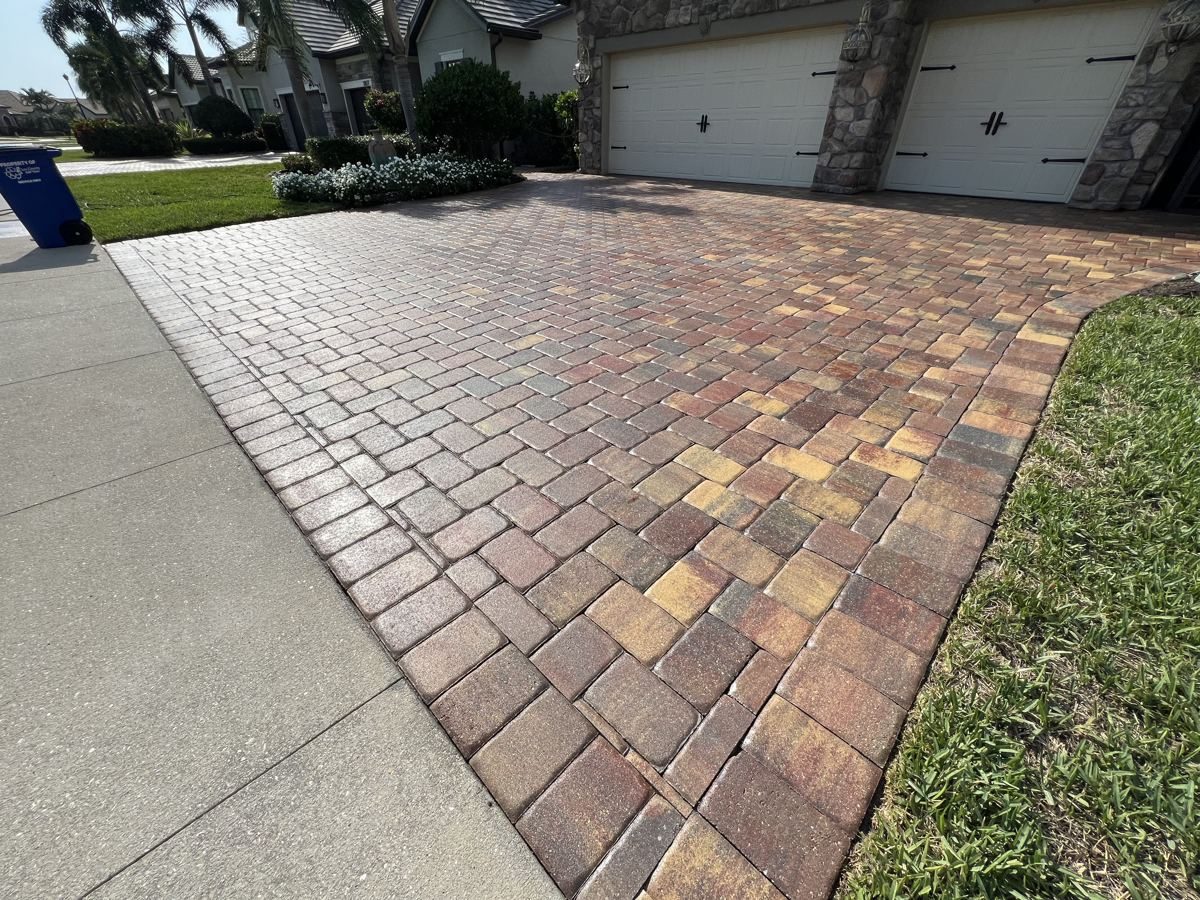 Freshly cleaned and sealed red, tan and charcoal paver driveway with a soldier-course border leading to a garage in Estero, FL