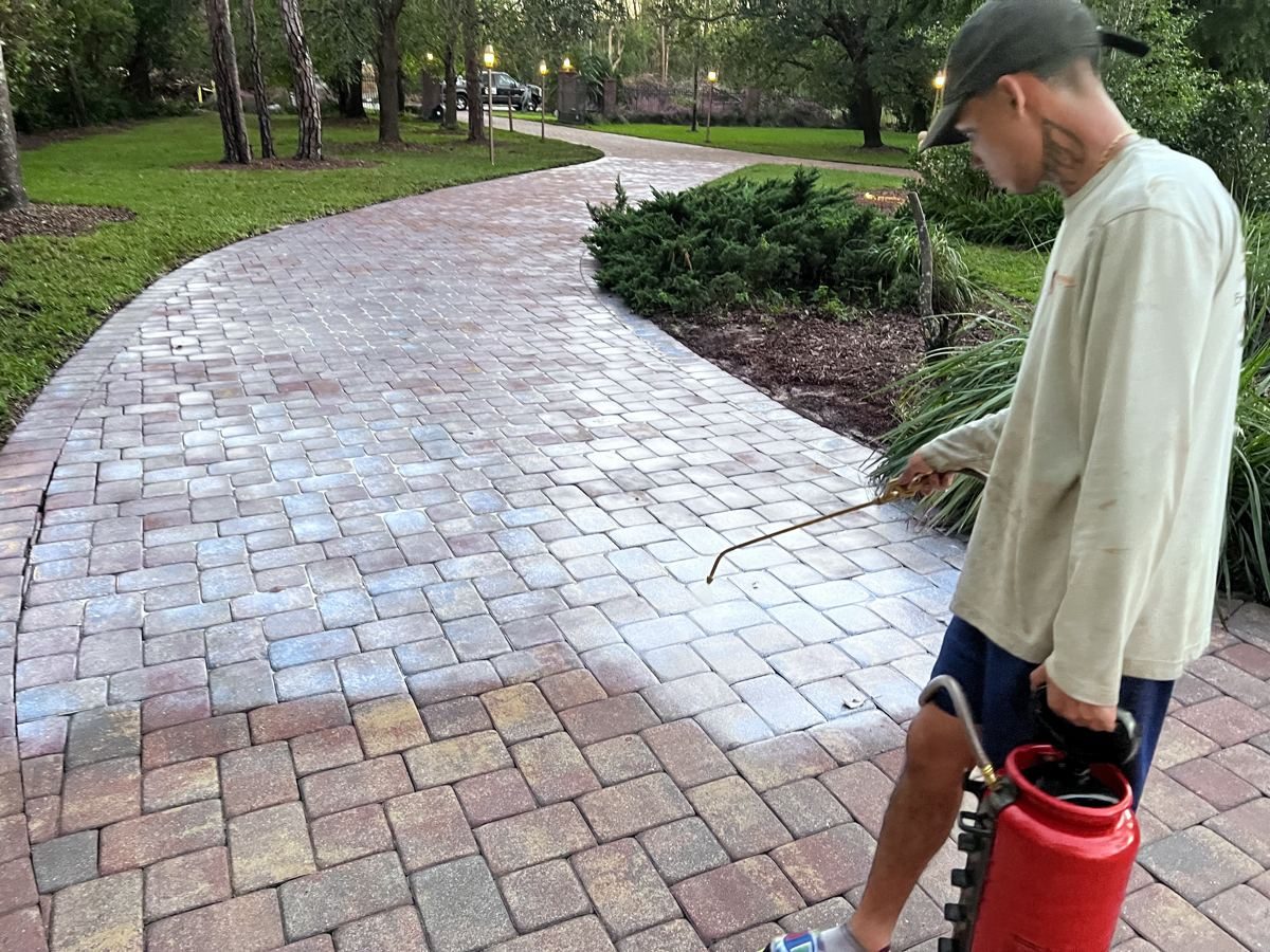Crew member applying sealer to a curved paver driveway with a red pump sprayer in Fort Myers, FL