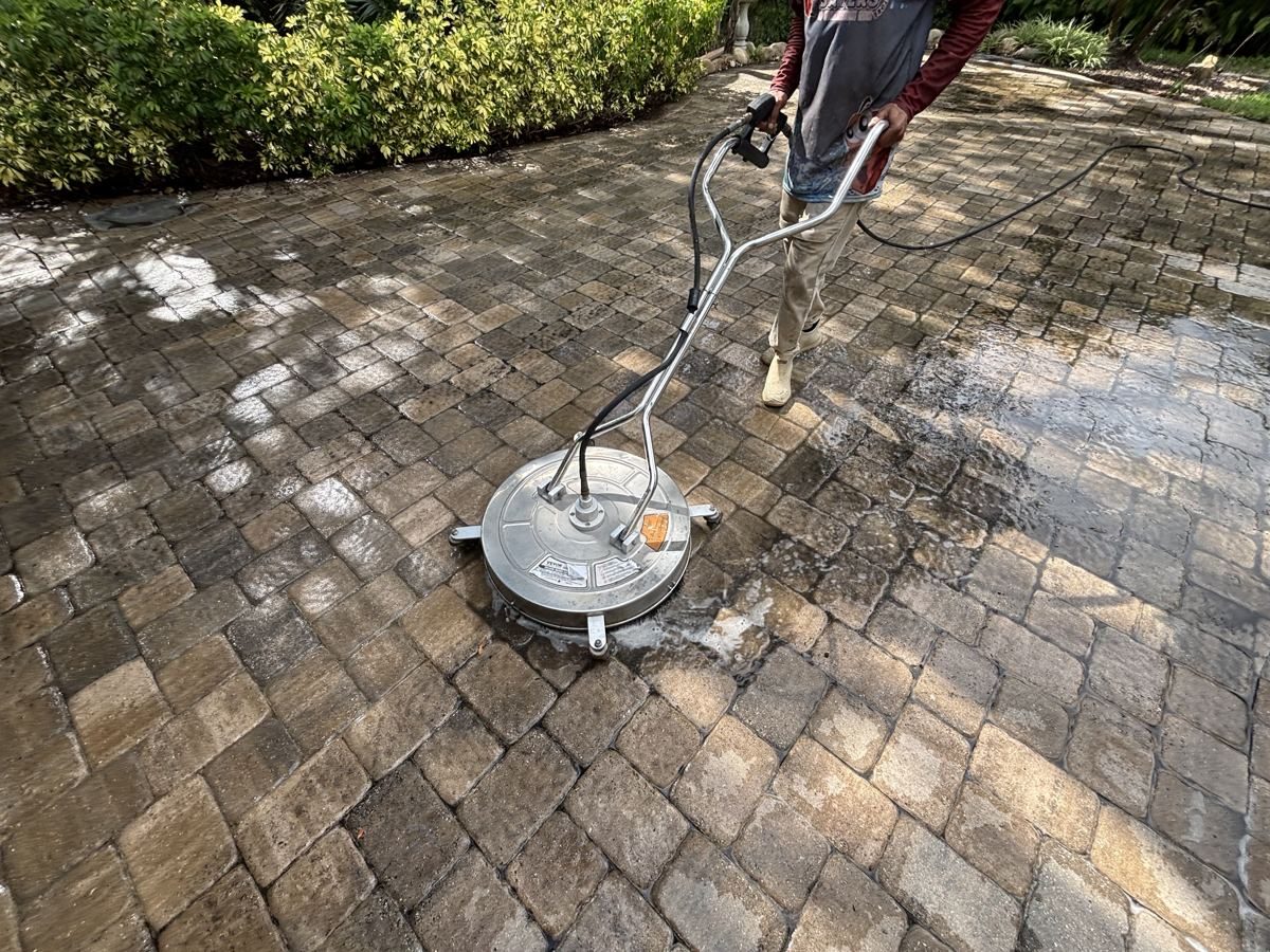 Crew member running a surface cleaner over dirty pavers, with cleaned and dirty sections side by side, in Fort Myers, FL