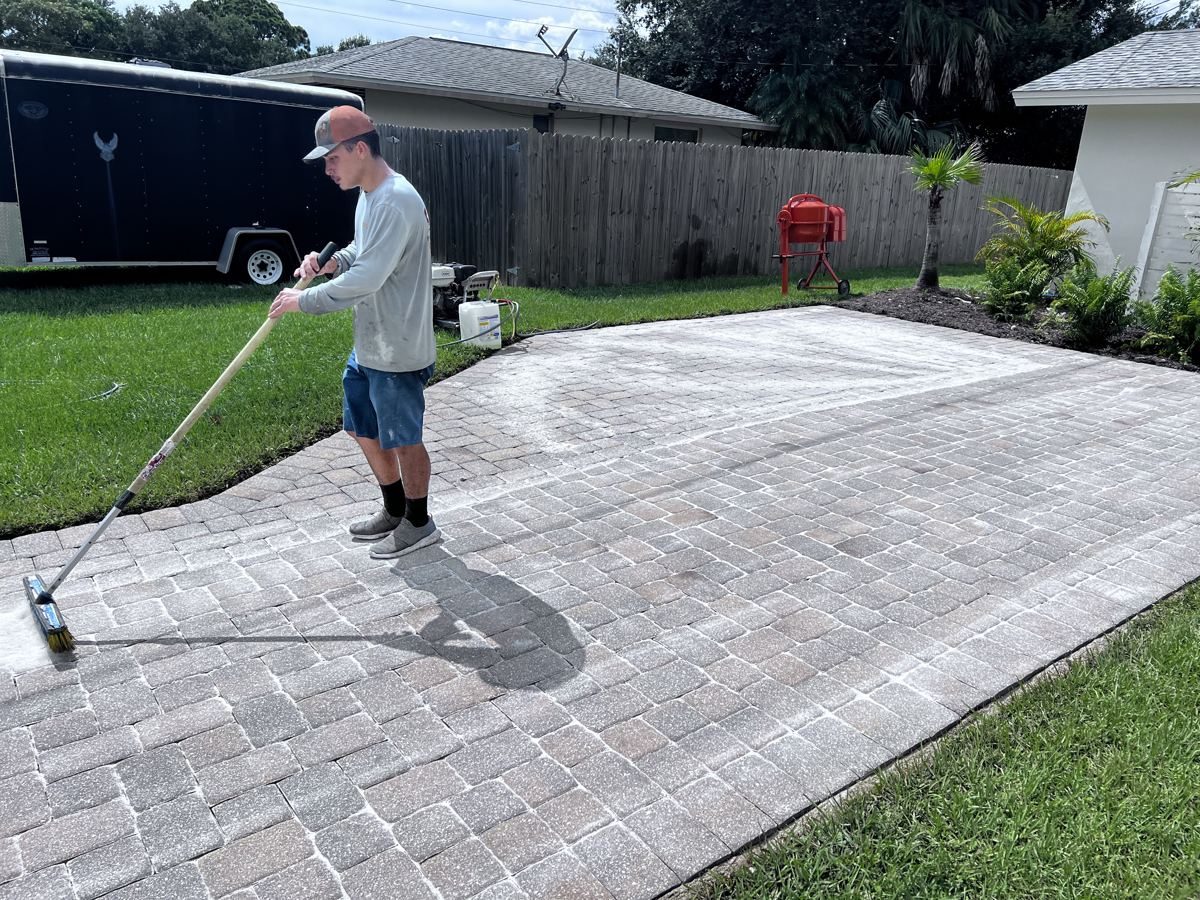 Crew member sweeping sand into the joints of a freshly cleaned paver driveway in Fort Myers, FL
