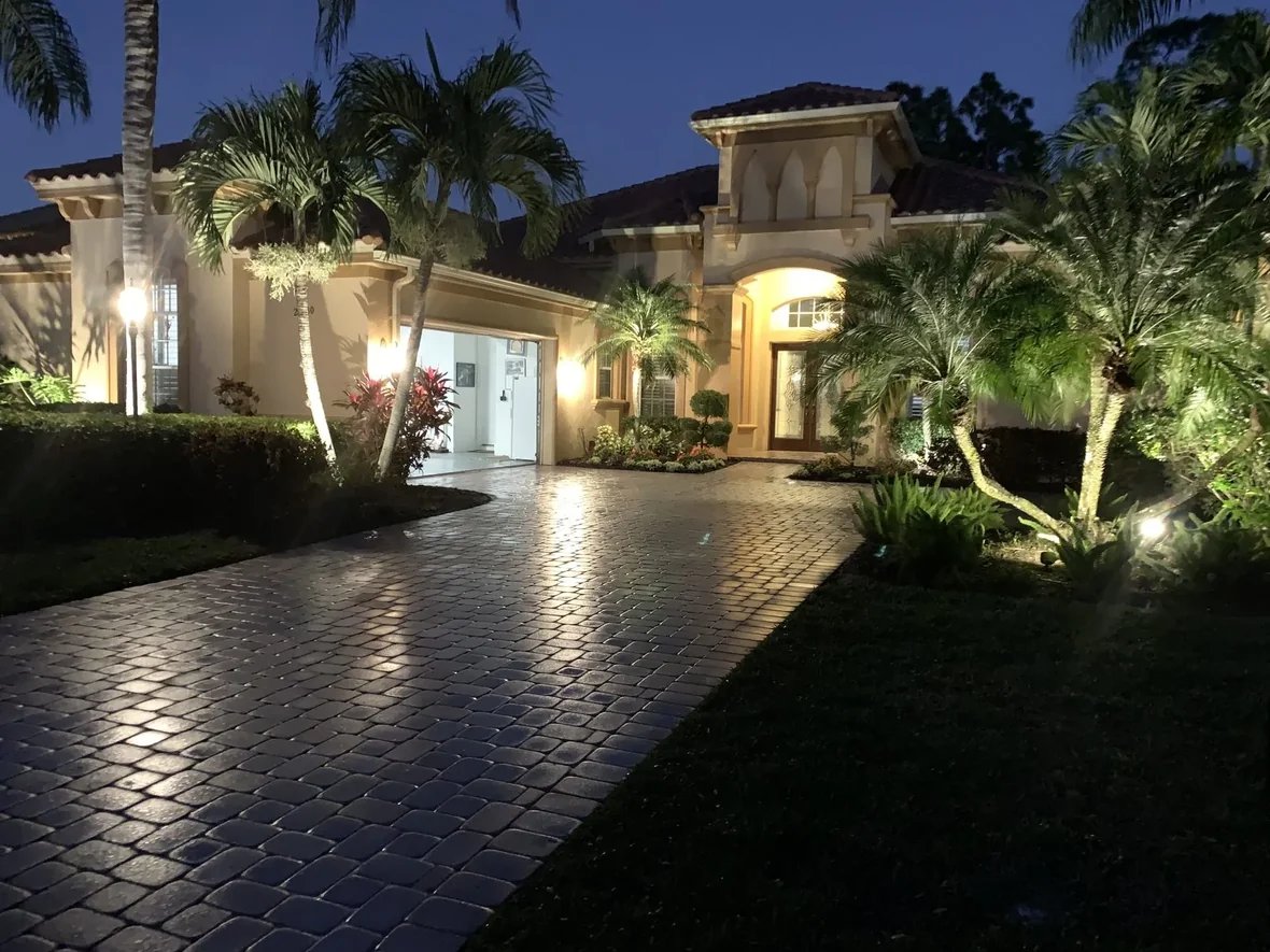 Sealed paver driveway with a glossy wet-look finish glowing under landscape lights at dusk in Bonita Springs, FL